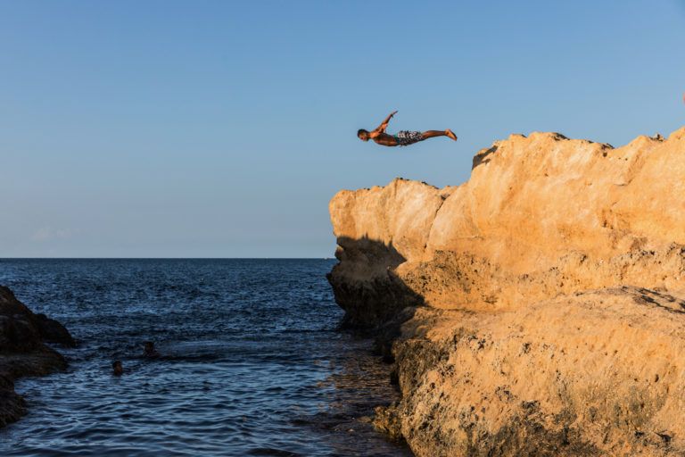 Young man jumping from rock to sea. Cliff Jumping into the Ocean at Sunset